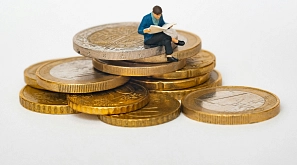 Miniaturfigur sitzt auf Münzen und liest