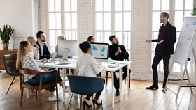 7 Menschen am Tisch verfolgen einen Vortrag